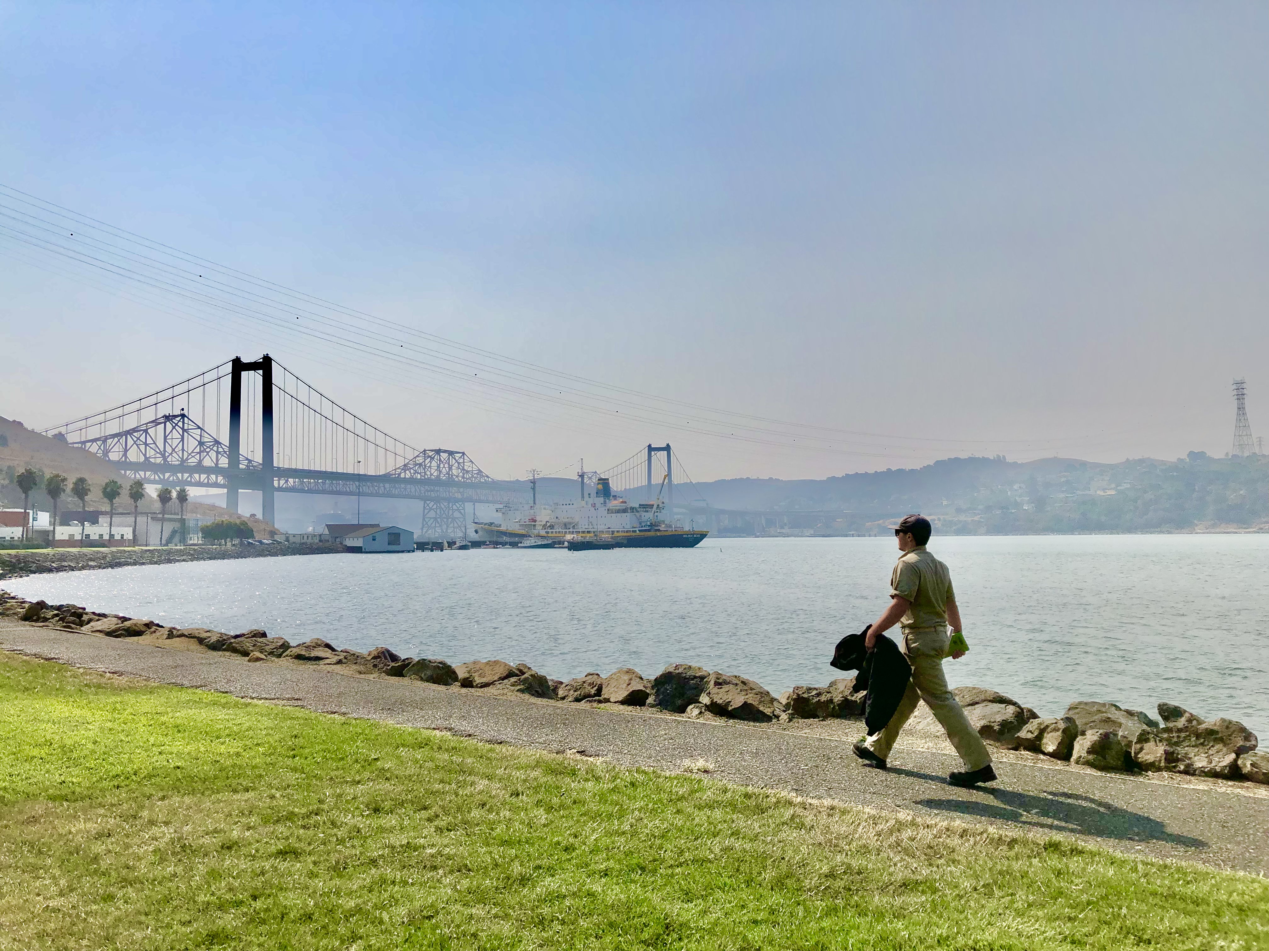A Cadet in khakis walks along the Cal Maritime campus waterfront