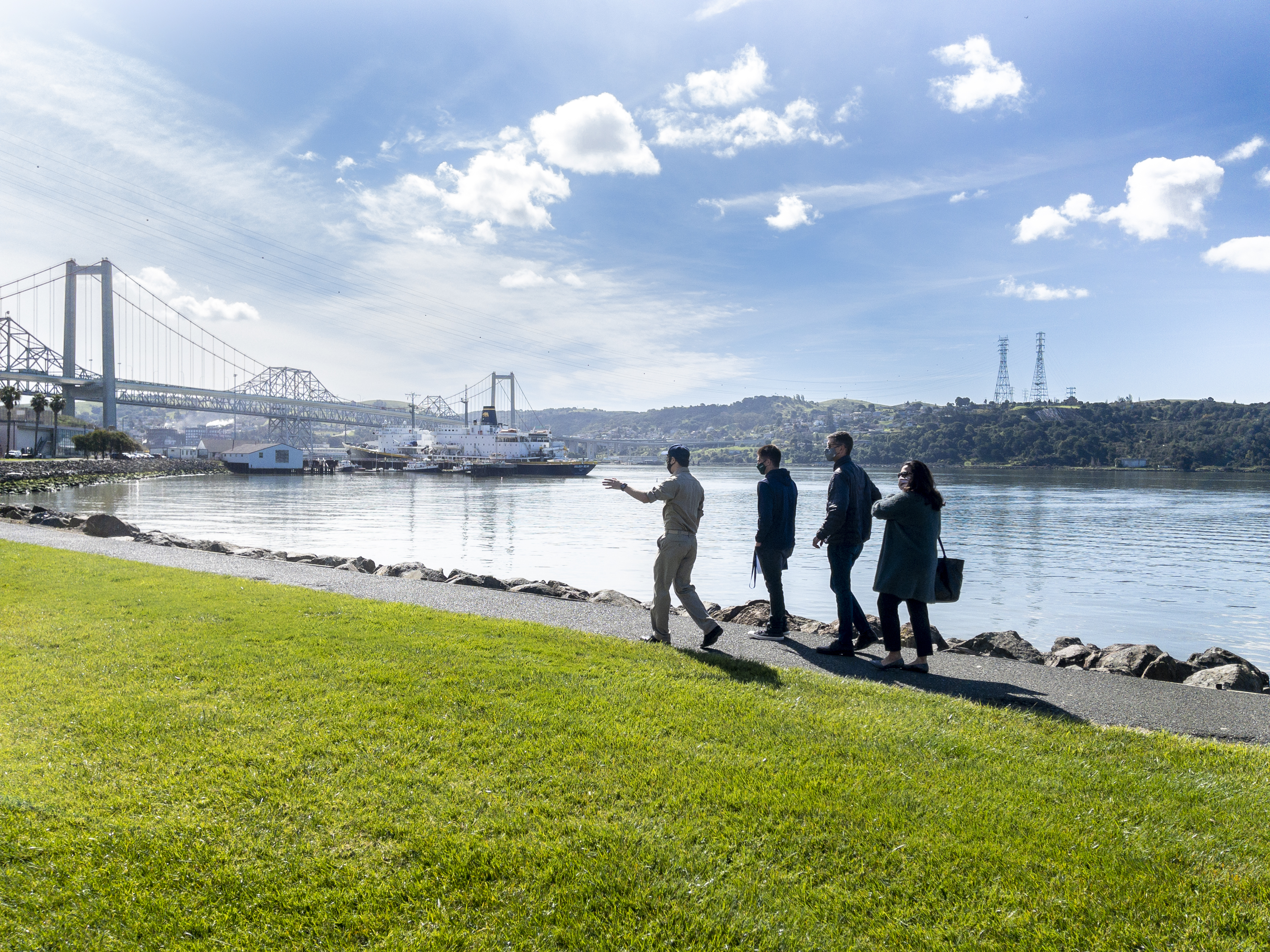 Family of 4 walks behind cadet tour guide along waterfront.