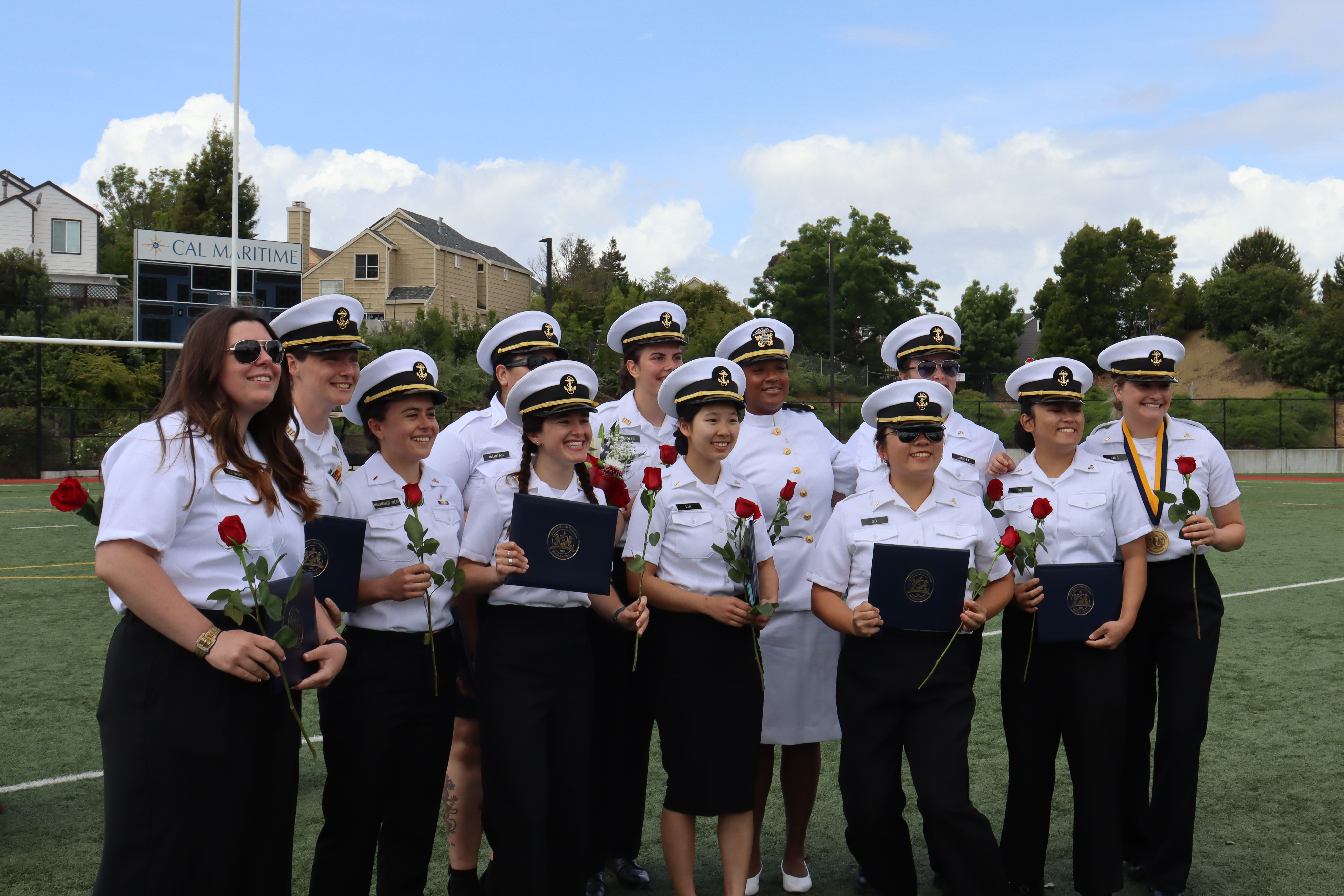 Recent graduates holding roses and diplomas smile at the camera during Commencement 2023.