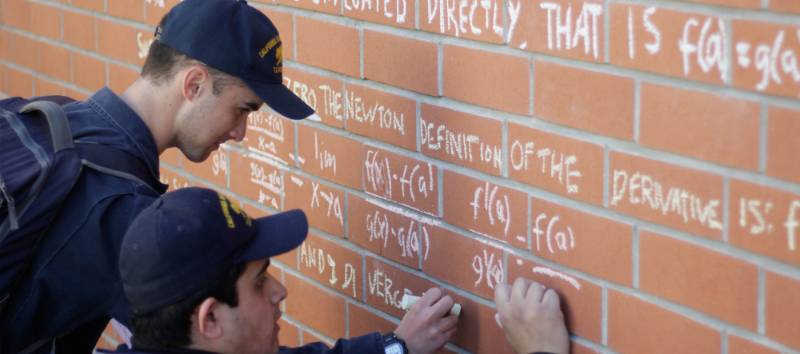 Students writing math calculations on a brick wall with chalk