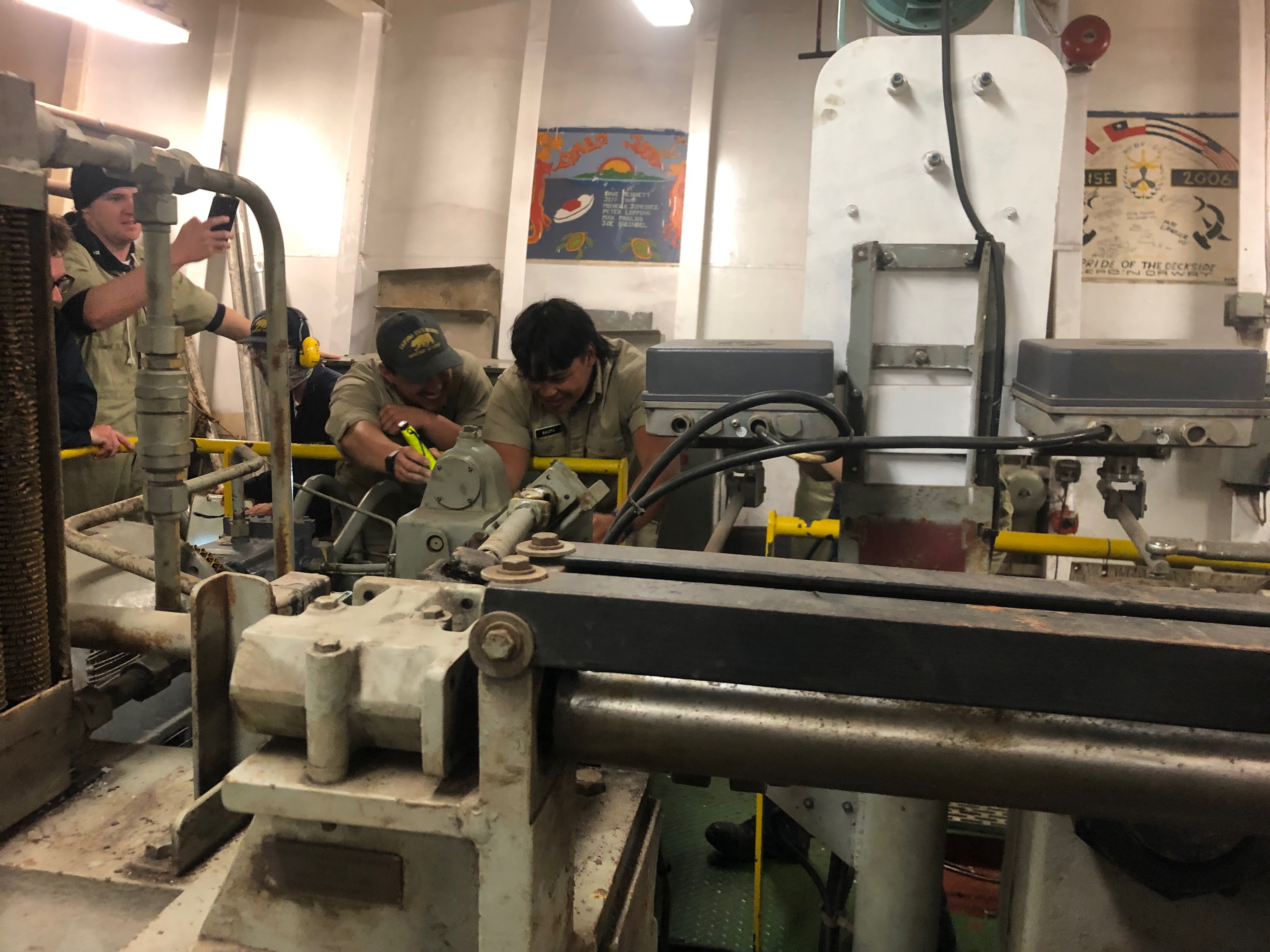 Cadet Third mate Solomon Kaupu controls the rudder while cadet second mate Danny Guzman lights the numbered notches behind the trick wheel 