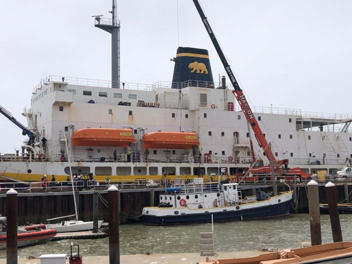 the crane is placing the one of the port lifeboats on the davits